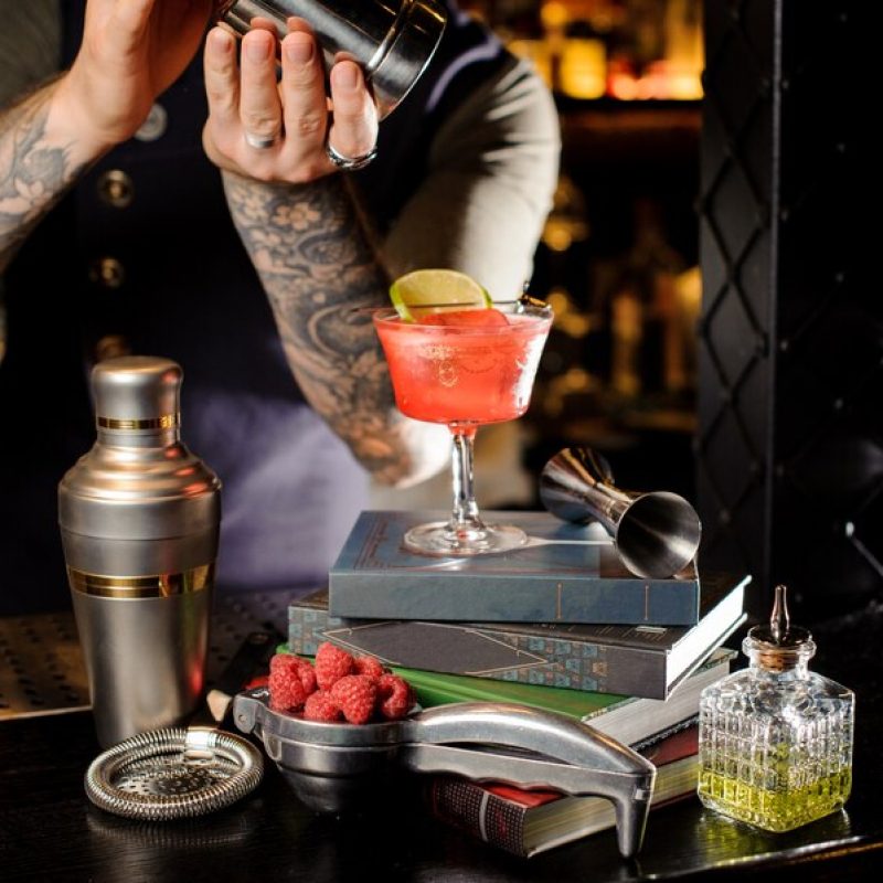 barman-making-fresh-sweet-red-sweet-summer-cocktail-arranged-books_130488-1976